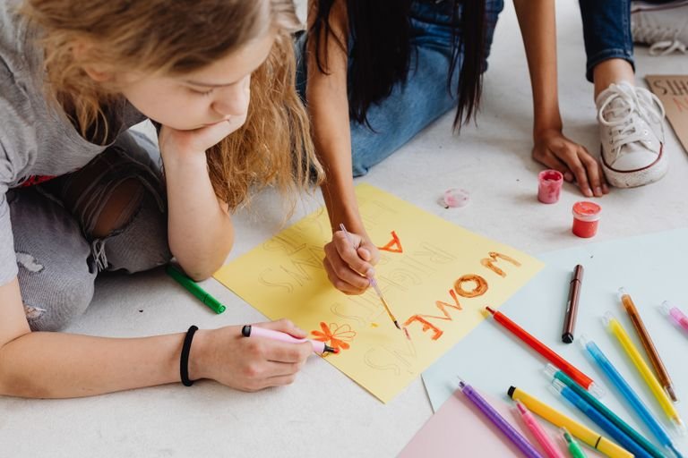 Teen girls creating colorful posters for activism, showcasing creativity and teamwork.